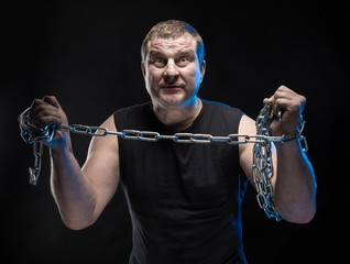 Actor Brutal man with a chain in his hands on a black background.