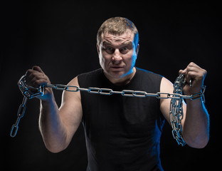 Actor Brutal man with a chain in his hands on a black background.