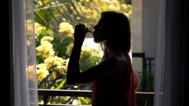 Silhouette of woman brushing teeth on terrace in garden, super slow motion 240fps
