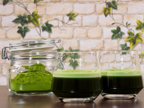 Two glasses of green juice and a jar of green juice powder