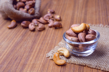 roasted cashew nuts with shell in gunny bag and on wooden background.