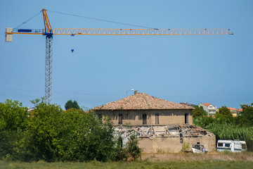 Fototapeta na wymiar Landscape with a dilapidated house and the tower crane. The eternal cycle of destruction and creation.