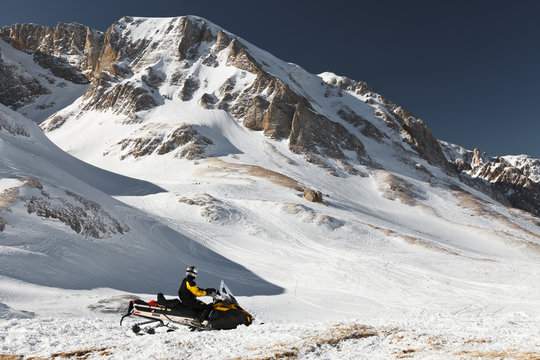 A man on a snowmobile against a background of snowy mountain peaks. State Nature Reserve in Adygea, Russia. 