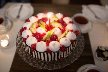 Delicious round chocolate cake with fruits on table, burning candle