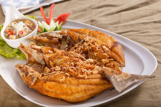 A dish of brown crispy deep fried whole sea bass fish with Thai style spicy dip sauce.