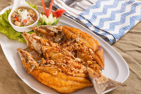 A dish of brown crispy deep fried whole sea bass fish with Thai style spicy dip sauce.