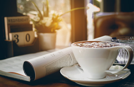 Cup of hot cappuccino with newspaper and calendar on the table,