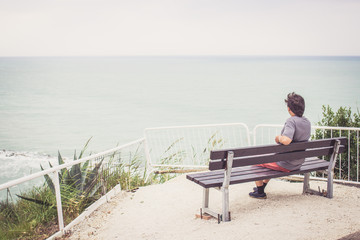 Young man sitting on bench overlooking sea