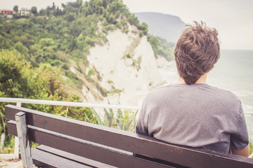 Young man sitting on bench overlooking sea