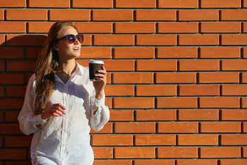 Young woman holding cup coffee near brick wall