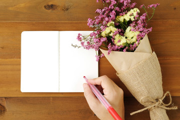 Hand writing on blank note book paper and flower bouquet on wood
