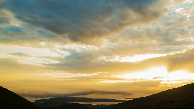 Idyllic timelapse shot of orange clouds rolling over silhouette mountains. Beautiful view of soft cloudscape moving in sky during sunset. Scenic view of tranquil nature. 4K resolution.

