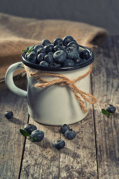 Fresh blueberries in enameled cup, rustic background, vintage filter, selective focus, still life