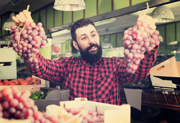 Smiling male seller offering grapes in shop