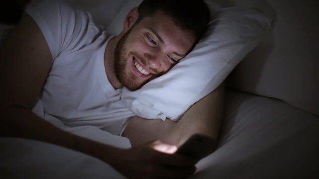 young man with smartphone in bed at night