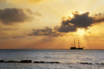 Ouderwetse zeilboot in piratenstijl die voorbijgaat aan de ondergaande zon bij Seven Mile Beach, Grand Cayman