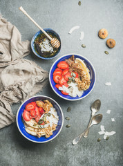 Yogurt, granola, seeds, fresh and dry fruits and honey in blue ceramic bowls over grey concrete background, top view, vertical composition. Clean eating, detox, dieting, vegetarian food concept