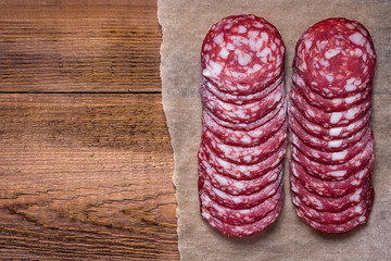 Sausage cut into circles on the paper. Natural wooden background. Blank space. View from above