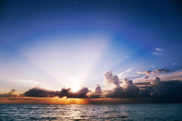 Zonnestralen waaieren uit de wolken bij zonsondergang boven Seven Mile Beach, Grand Cayman