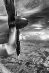 Black and white vertical view of an airplane propeller in flight with Tuscan countryside background