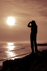 Fototapeta premium Silhouetted female figure shields her eyes as she looks at the s