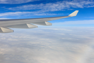 Fototapeta premium A view of wing of airplane from window above clouds and blue sky