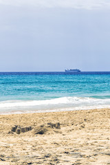 Fototapeta na wymiar Sommerlandschaft am Strand aus Fuerteventura, Kanaren mit einer beschädigten Sandburg und erstaunliche Farbe des Ozeans und ein Schiff im Hintergrund.