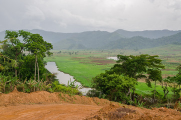 River and dirt road with mountains and lush vegetation at Ring Road in Cameroon, Africa