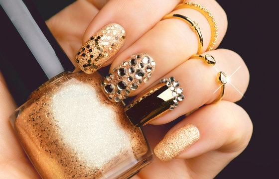 Fototapeta Golden nail art manicure. Holiday style bright manicure with gems and sparkles. Bottle of nail Polish. Fashion rings