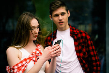 Two happy trendy teenage friends walking and dancing in the city, listening to the music with headphones, talking each other and smiling. Lifestyle, friendship and urban life concepts.