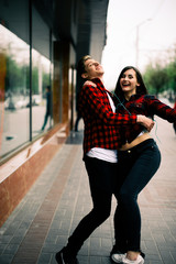 Obraz premium Two happy trendy teenage friends walking and dancing in the city, listening to the music with headphones, talking each other and smiling. Lifestyle, friendship and urban life concepts.