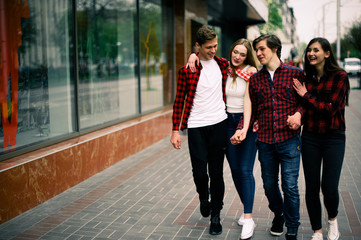 Four happy trendy teenage friends walking in the city, talking each other and smiling. Lifestyle, friendship and urban life concepts.