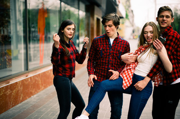 Two happy trendy teenage friends walking and dancing in the city, listening to the music with headphones, talking each other and smiling. Lifestyle, friendship and urban life concepts.