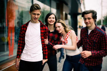 Four happy trendy teenage friends walking in the city, talking each other and smiling. Lifestyle, friendship and urban life concepts.