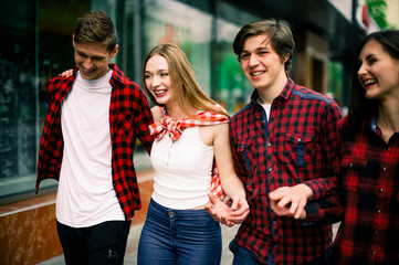 Four happy trendy teenage friends walking in the city, talking each other and smiling. Lifestyle, friendship and urban life concepts.