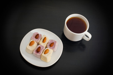 Cup of tea, saucer with Turkish Delight on a black table, top view