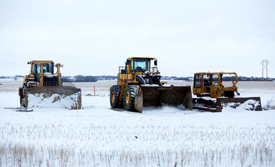 An industrial loader with bucket and two bulldozers prepared for snow removal parked on a snow...