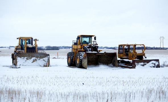 An industrial loader with bucket and two bulldozers prepared for snow removal parked on a snow covered field in winter landscape