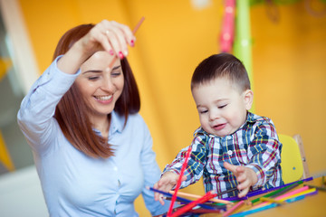 Portrait of happy pretty mother with her toddler son drawing