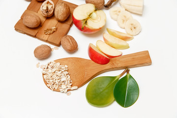 There are Banana,Apple,Walnuts and Rolled Oats,Wooden Spoon,Trivet,with Green Leaves,Healthy Fresh Organic Food on the White Background,Top View