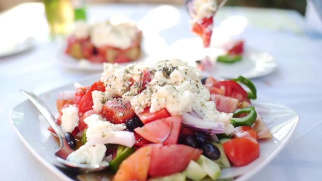 picking with a fork from a greek salade in a Mediterranean  summer setting