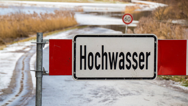 Road barrier with flood warning sign in front of flooded road in germany