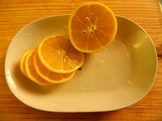 on light wood chopping board is a white oblong dish with chopped fresh lemon rings with stones on a horizontal surface top view