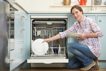 Woman Loading Dishwasher In Kitchen