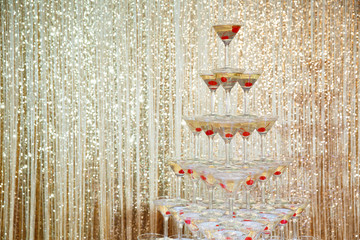 Sparkling champagne pyramid, tower of glasses at the party in front of golden wall