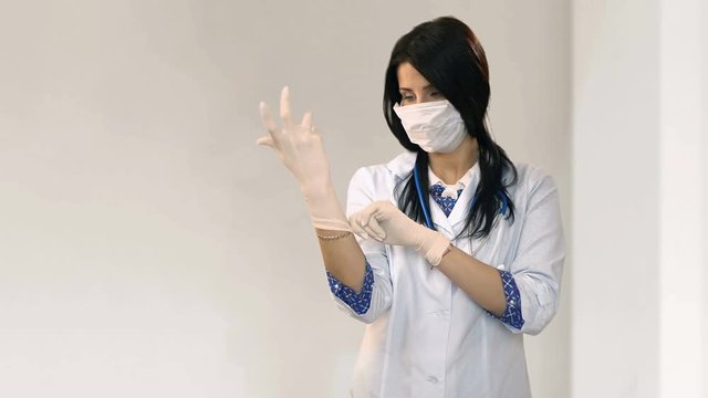 Attractive doctor puts on gloves in white room