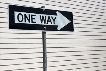 ONE WAY sign with light beige clapboard wall background. Horizontal.