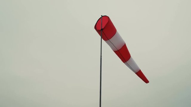 Red and white windsock wind filled gray sky background.