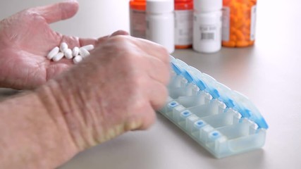 Elderly man counts out his medication and vitamins for the week using a daily pill box.