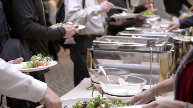 Guests attending a corporate business seminar in a hotel help themselves to the free hot lunch at the catered buffet table.